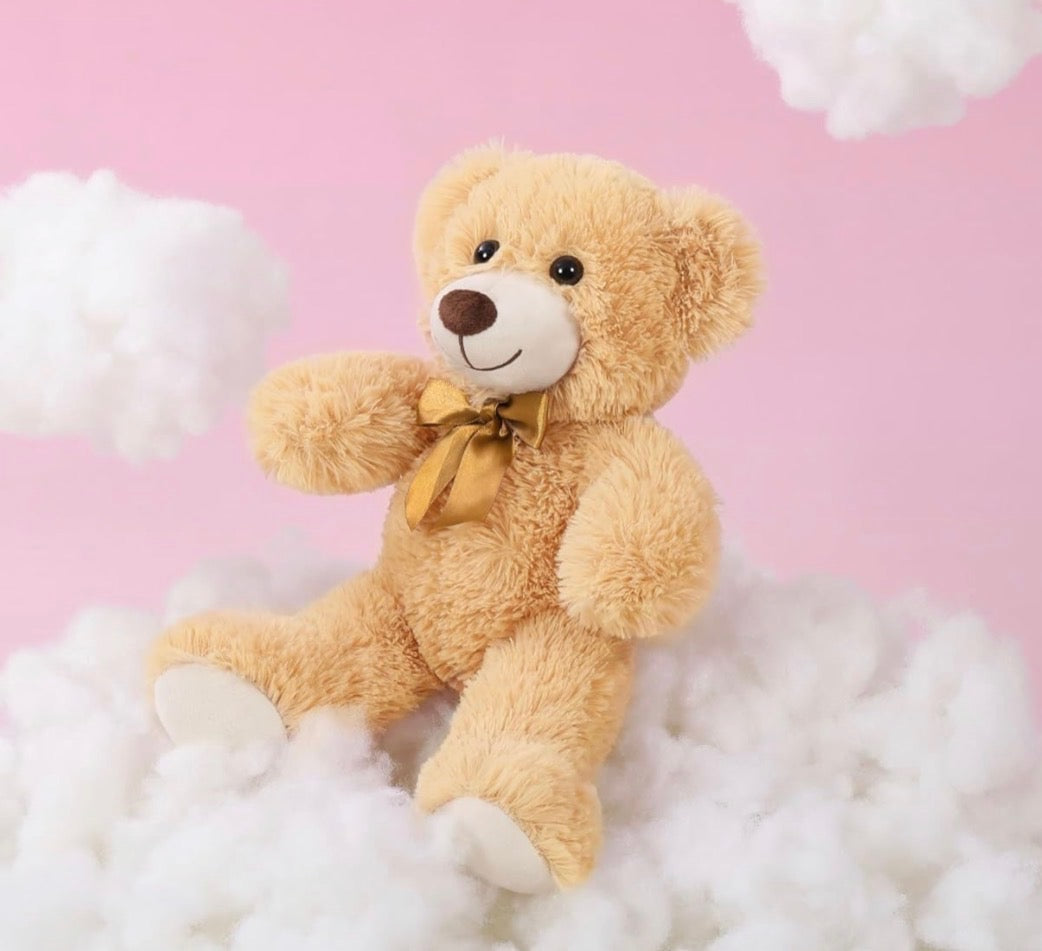 Teddy bear with a gold bow sitting on fluffy white clouds against a pink background